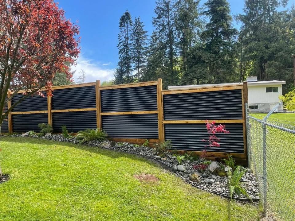 Modern wood and corrugated-metal privacy fence with red Japanese maple and rock garden border