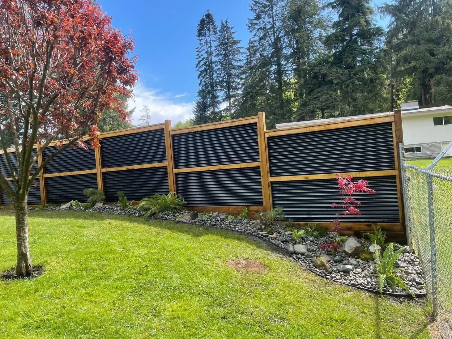 Long modern wood and corrugated-metal privacy fence with a Japanese maple under a clear blue sky
