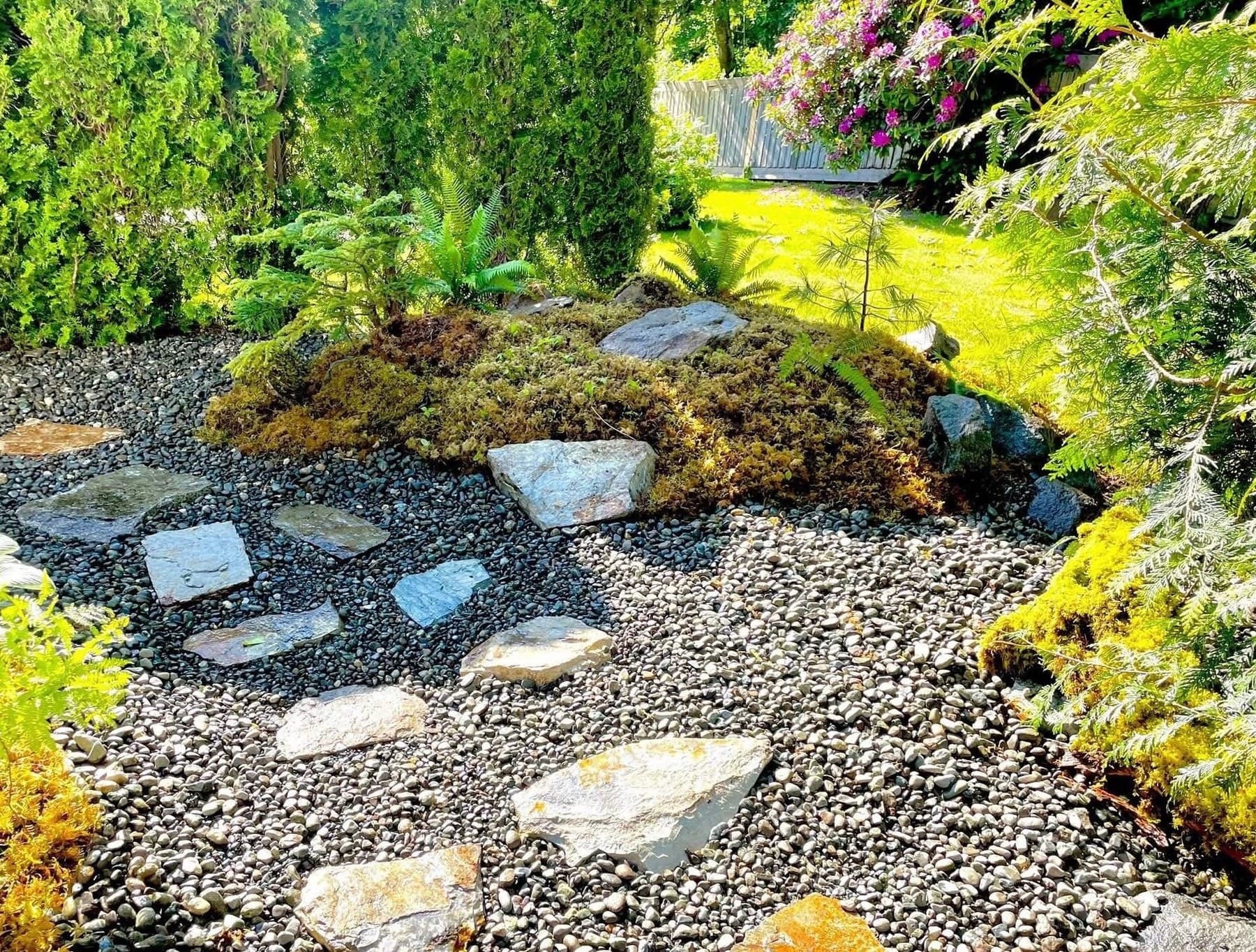 Stepping-stone path through a gravel garden with mossy boulders and surrounding cedars