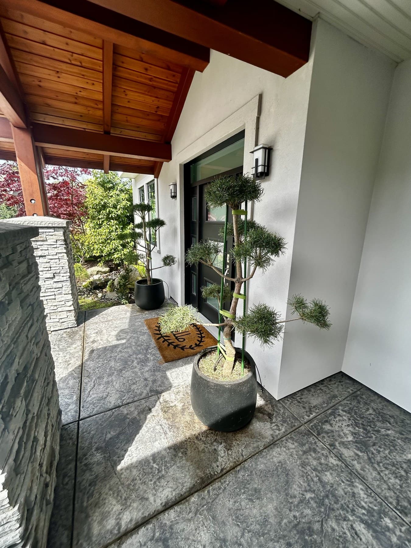 Modern entrance with a single sculpted topiary in a stone planter and stone-clad columns